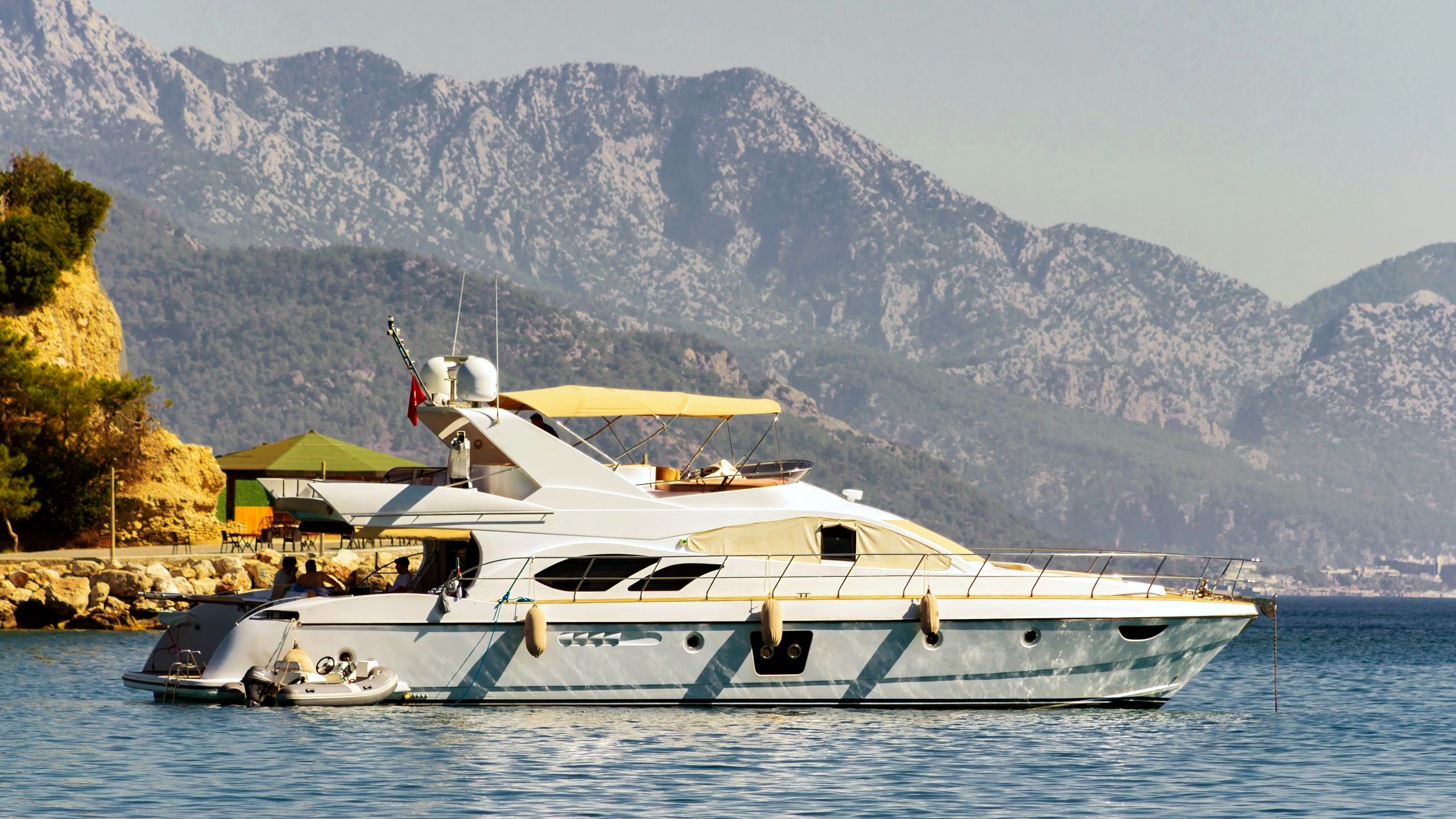Luxury yacht on calm blue water with dramatic coastal mountains